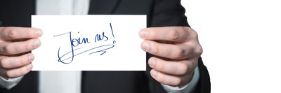 man holding a piece of paper with Join Us written on it